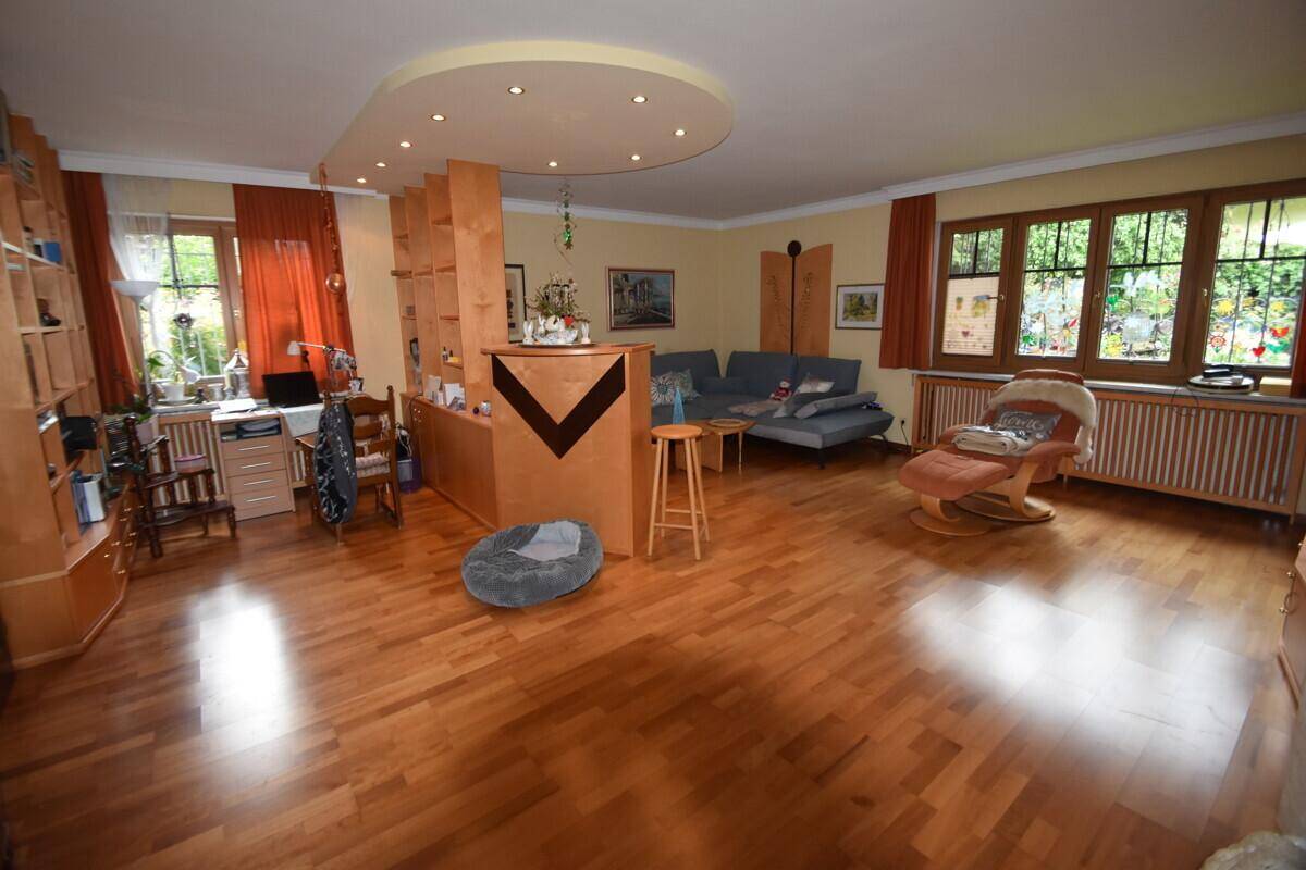 Helles Wohnzimmer mit Parkettboden, großen Fenstern und vielseitigen Möbeln.