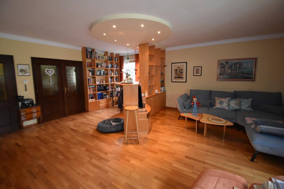 Geräumiges Wohnzimmer mit Parkettboden, gemütlicher Couch und integriertem Bücherregal.