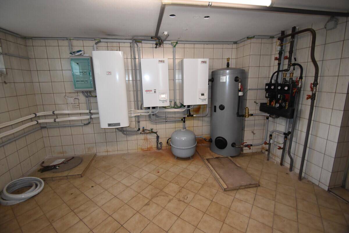 Technikraum im Keller mit Heizungsanlagen und Warmwasserspeicher, funktional eingerichtet.