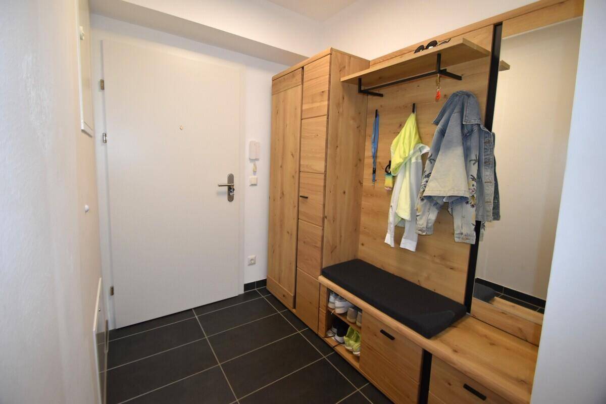 Heller Eingangsbereich mit Holzgarderobe, Sitzbank und dunklen Fliesen.