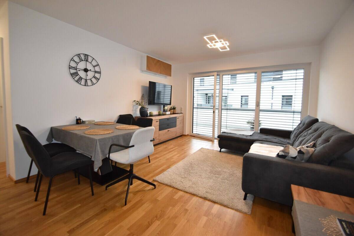 Heller Wohn- und Essbereich mit Holzboden, Sofa und Zugang zum Balkon.