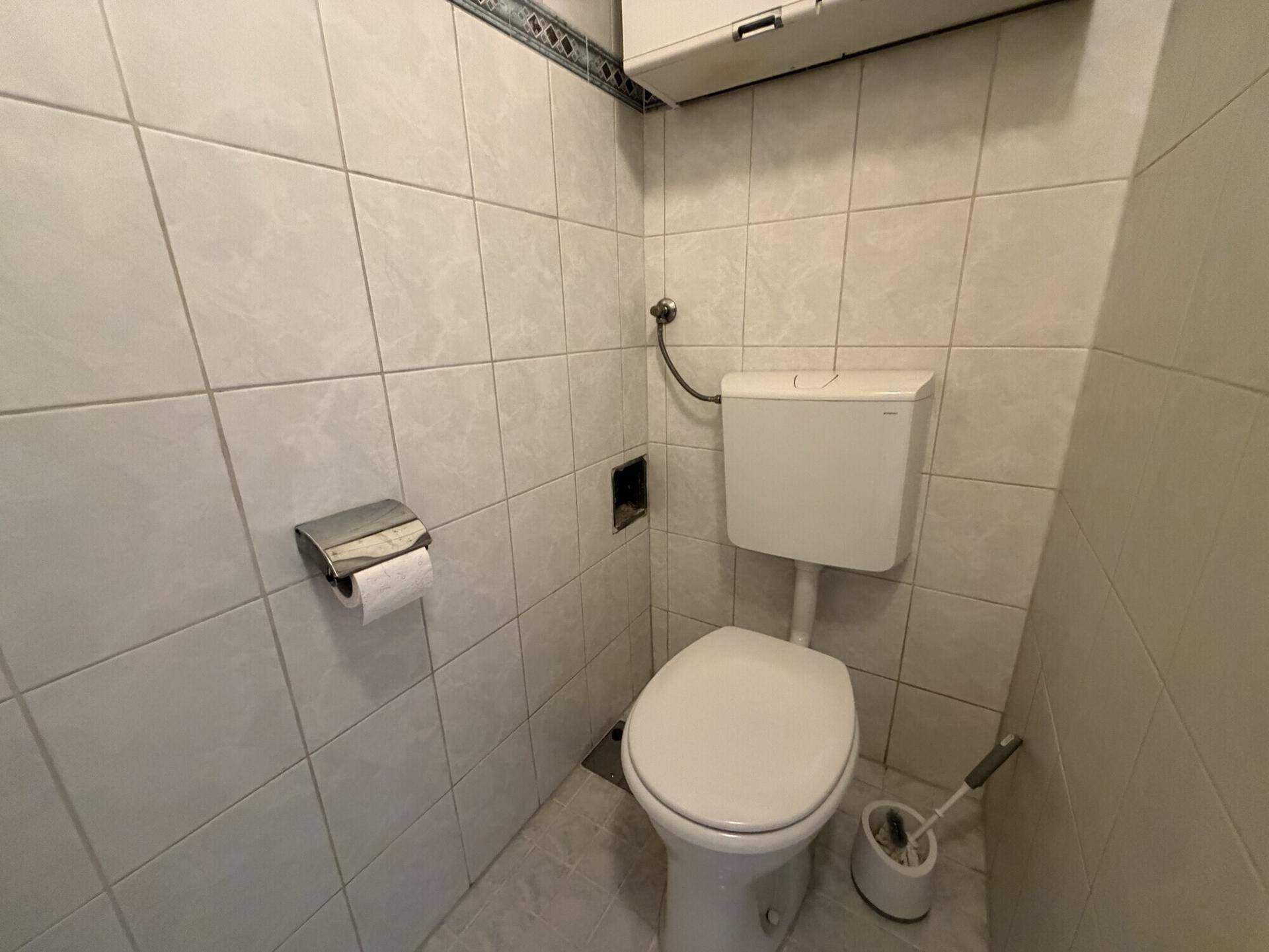 Separates WC mit weißen Fliesen und Standard-Toilette.