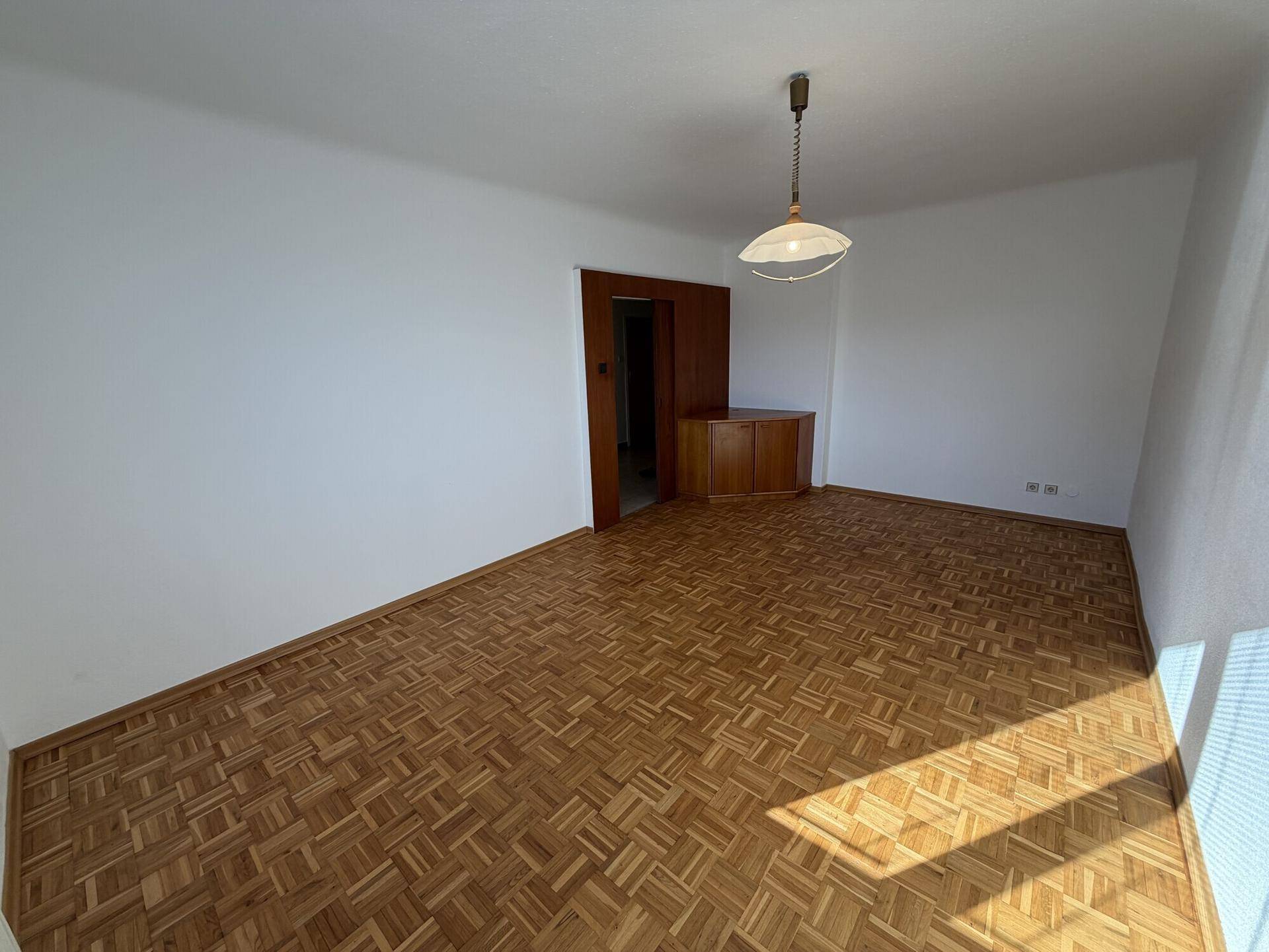 Geräumiges Zimmer mit klassischem Parkettboden und Zugang zu weiteren Räumen.