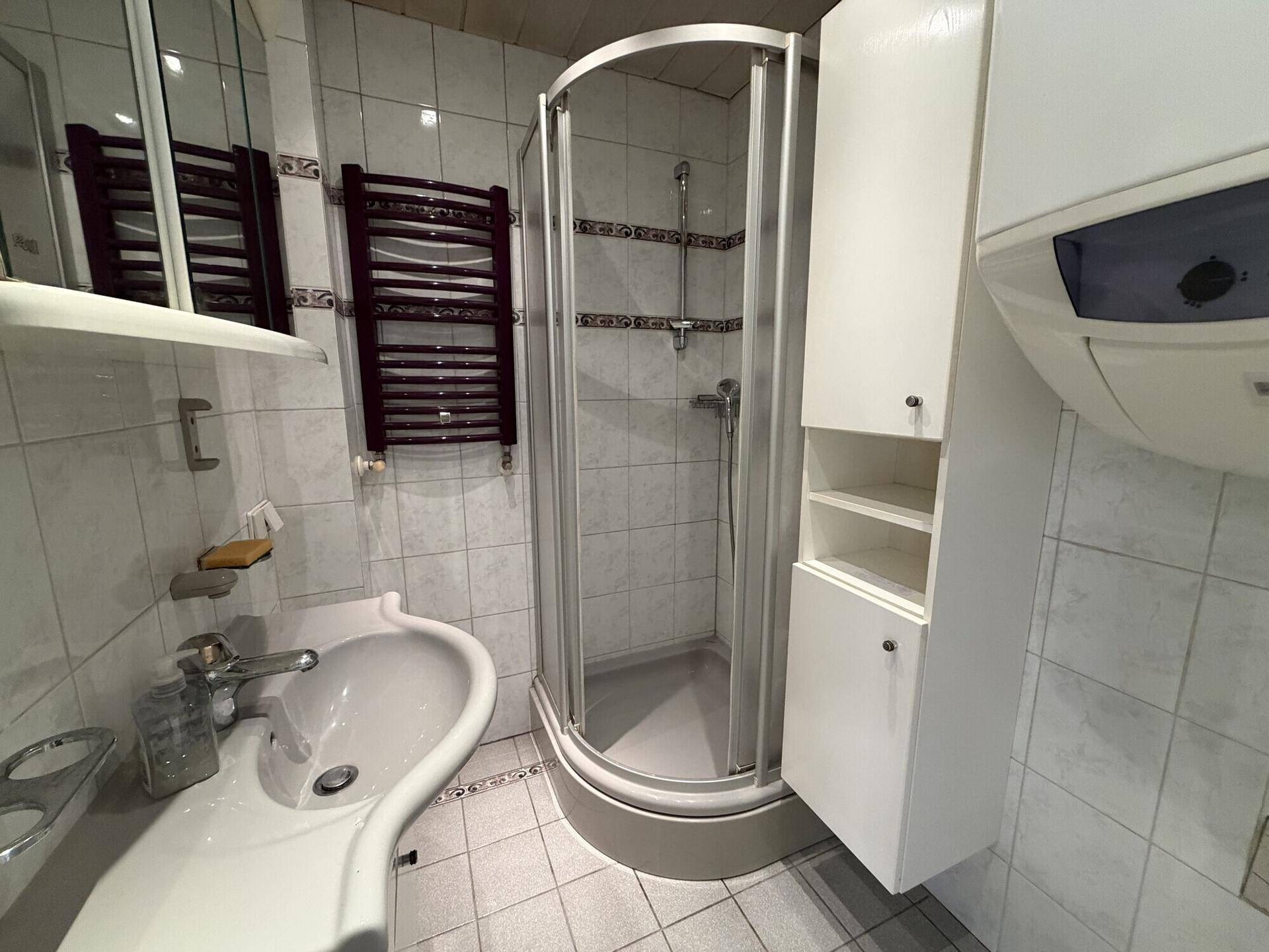 Gefliestes Badezimmer mit Dusche, Waschbecken und beheiztem Handtuchhalter.