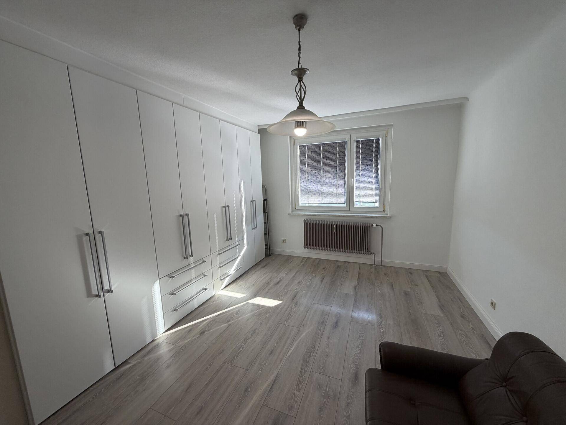 Helles Zimmer mit modernem Laminatboden und großen weißen Einbauschränken.
