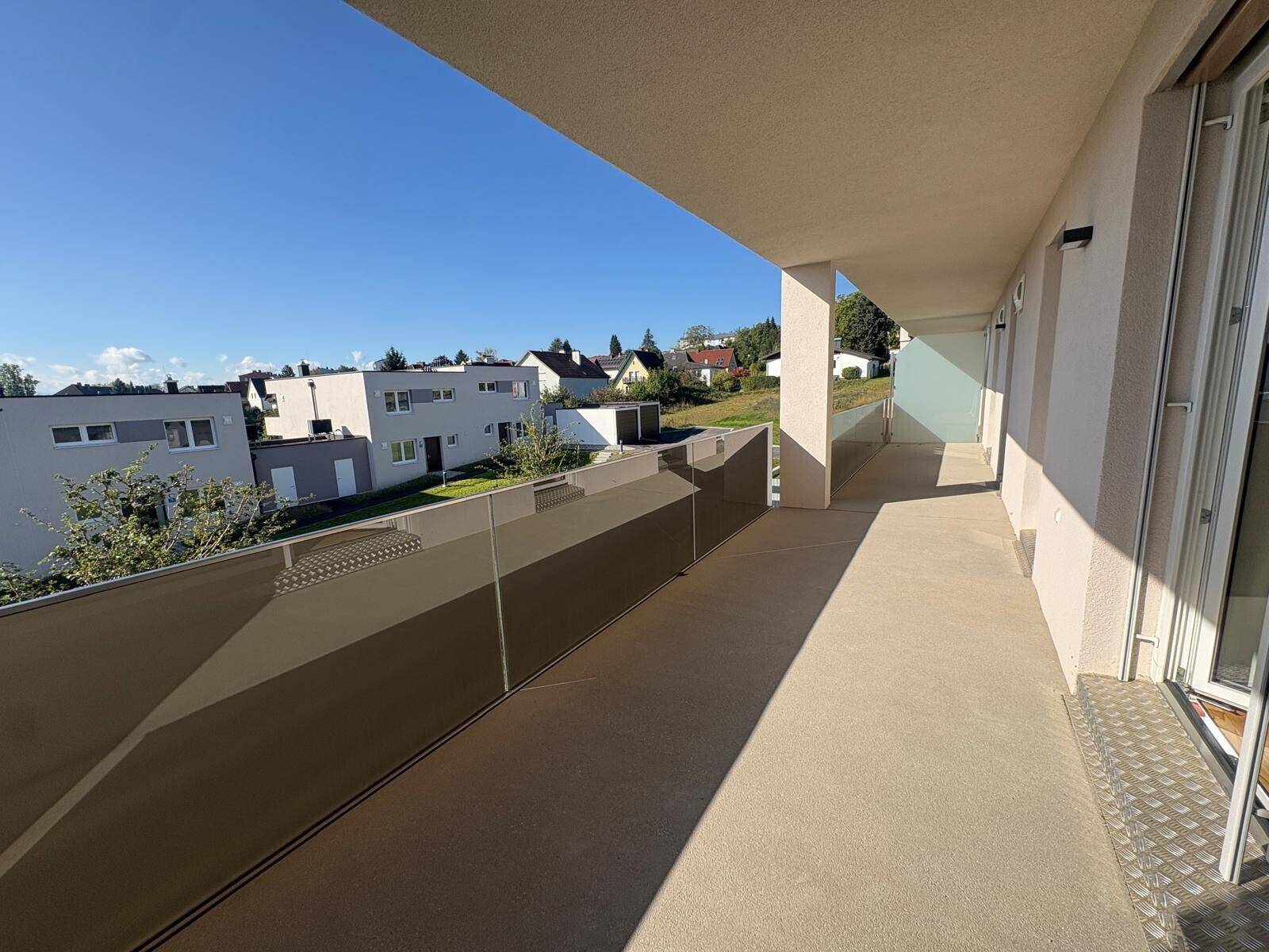 Langer, sonniger Balkon mit Glasbrüstung und Blick auf die umliegende Wohngegend.