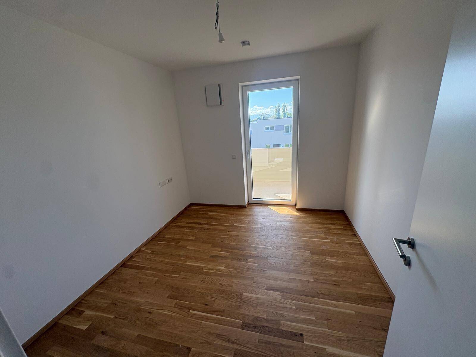 Unmöbliertes Zimmer mit Parkettboden und großer Fenstertür, ideal als Schlaf- oder Arbeitszimmer.