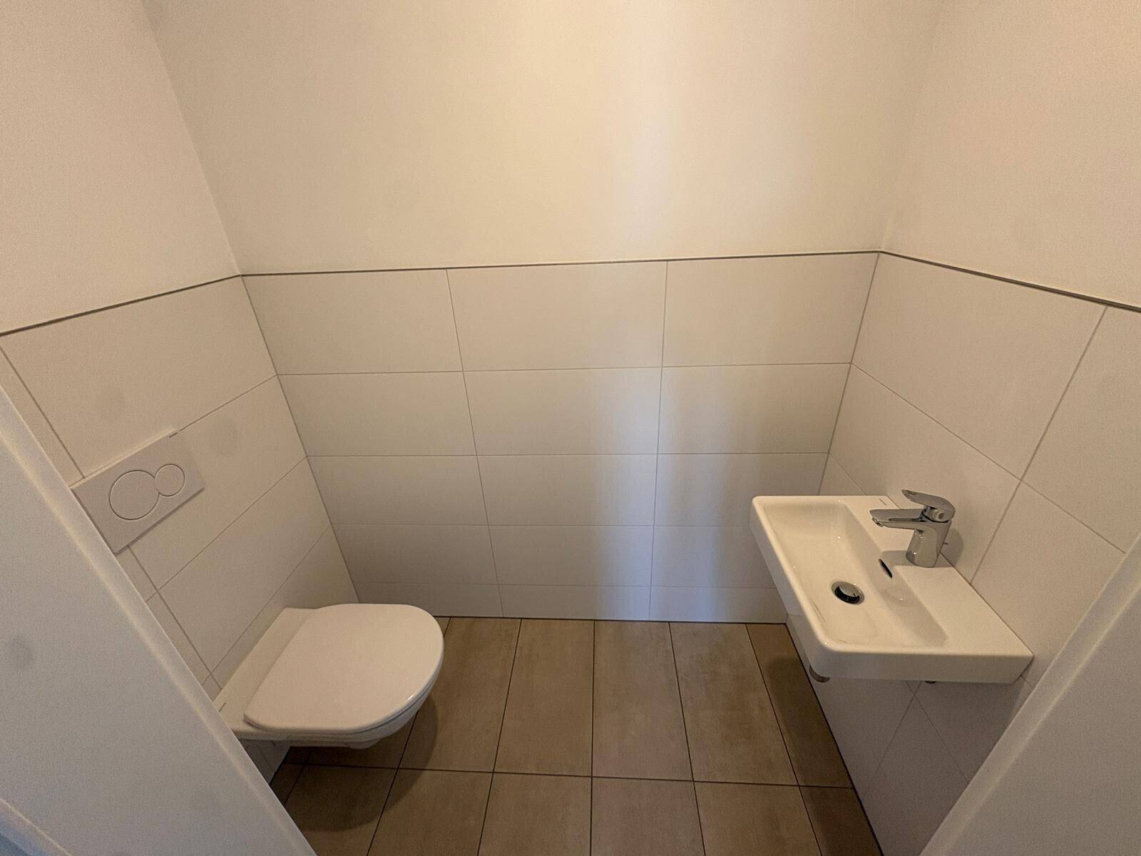 Kleines Gäste-WC mit Wand-WC, Handwaschbecken und hellen Fliesen an Wänden und Boden.