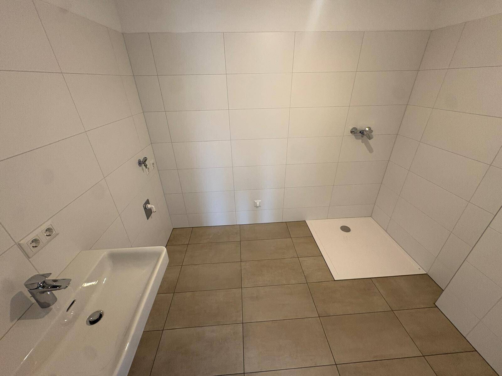 Modernes Badezimmer im Bau mit weißen Fliesen, Einzelwaschbecken und bodengleicher Dusche.