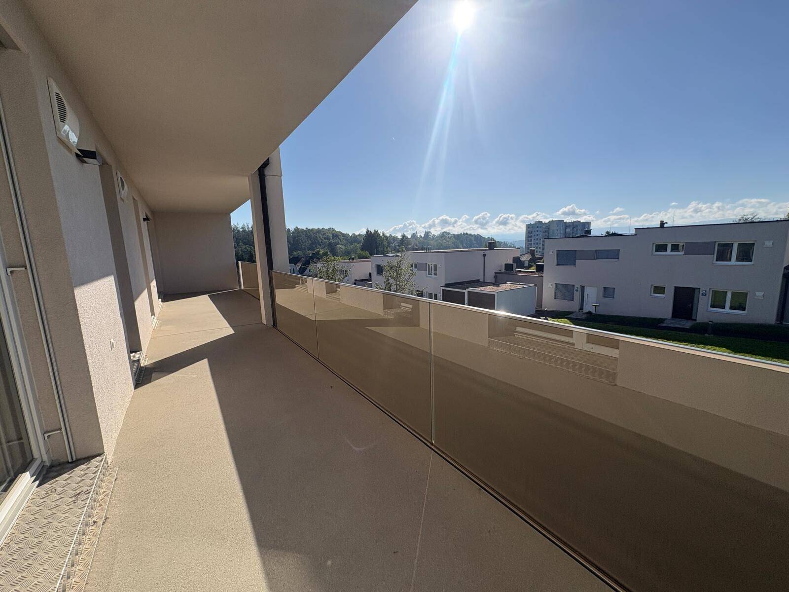 Sonniger Balkon mit moderner Glasbrüstung und weitem Blick über die Dächer der Nachbarschaft.