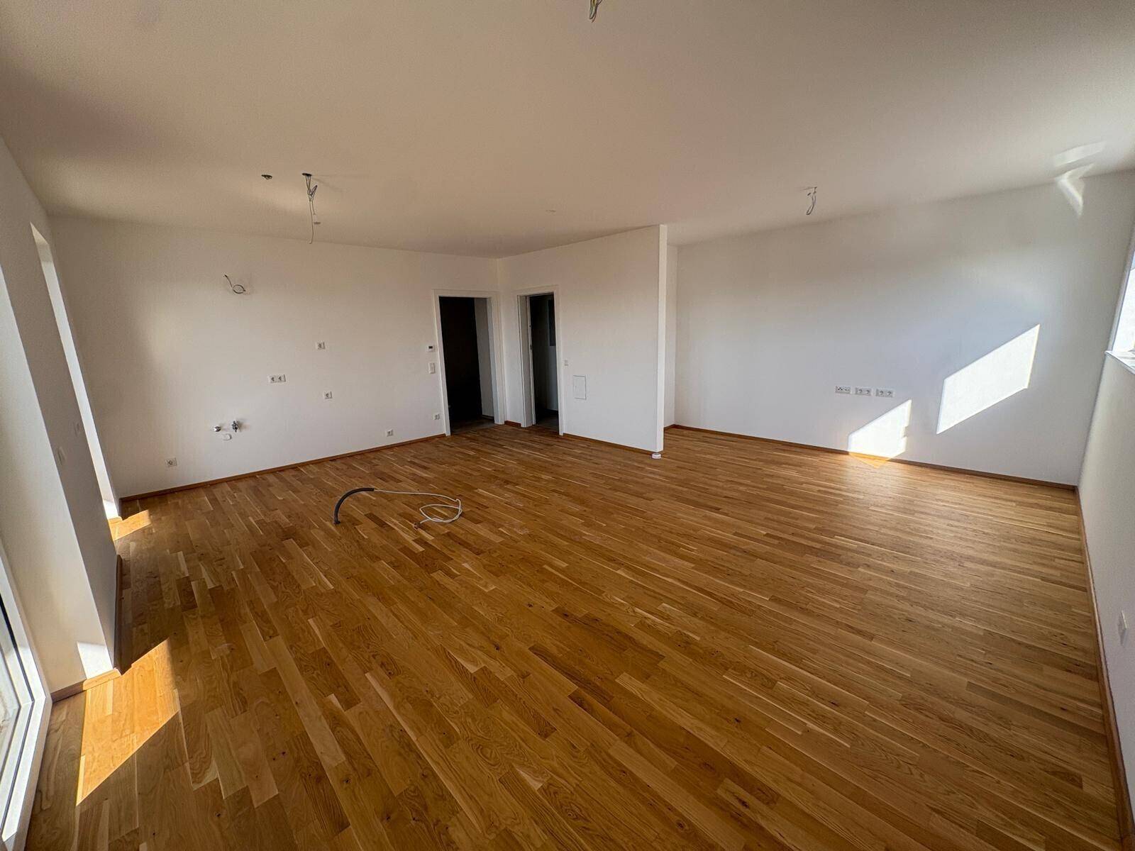 Geräumiger, unmöblierter Wohnbereich mit hellem Parkettboden und Zugang zu weiteren Räumen.