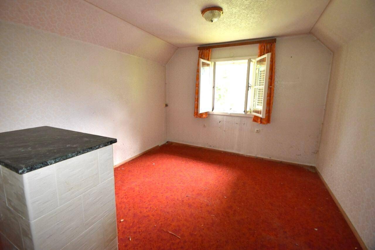 Dachschlafzimmer mit rotem Teppichboden, einem kleinen Fenster und einem gemauerten Ofen für Wärme.
