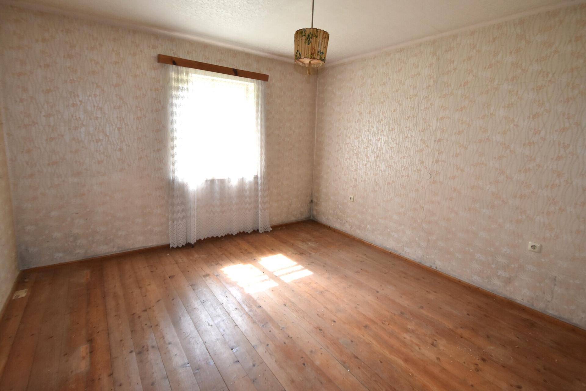 Schlafzimmer mit Holzdielenboden, gemusterter Tapete und einem großen Fenster für viel Tageslicht.