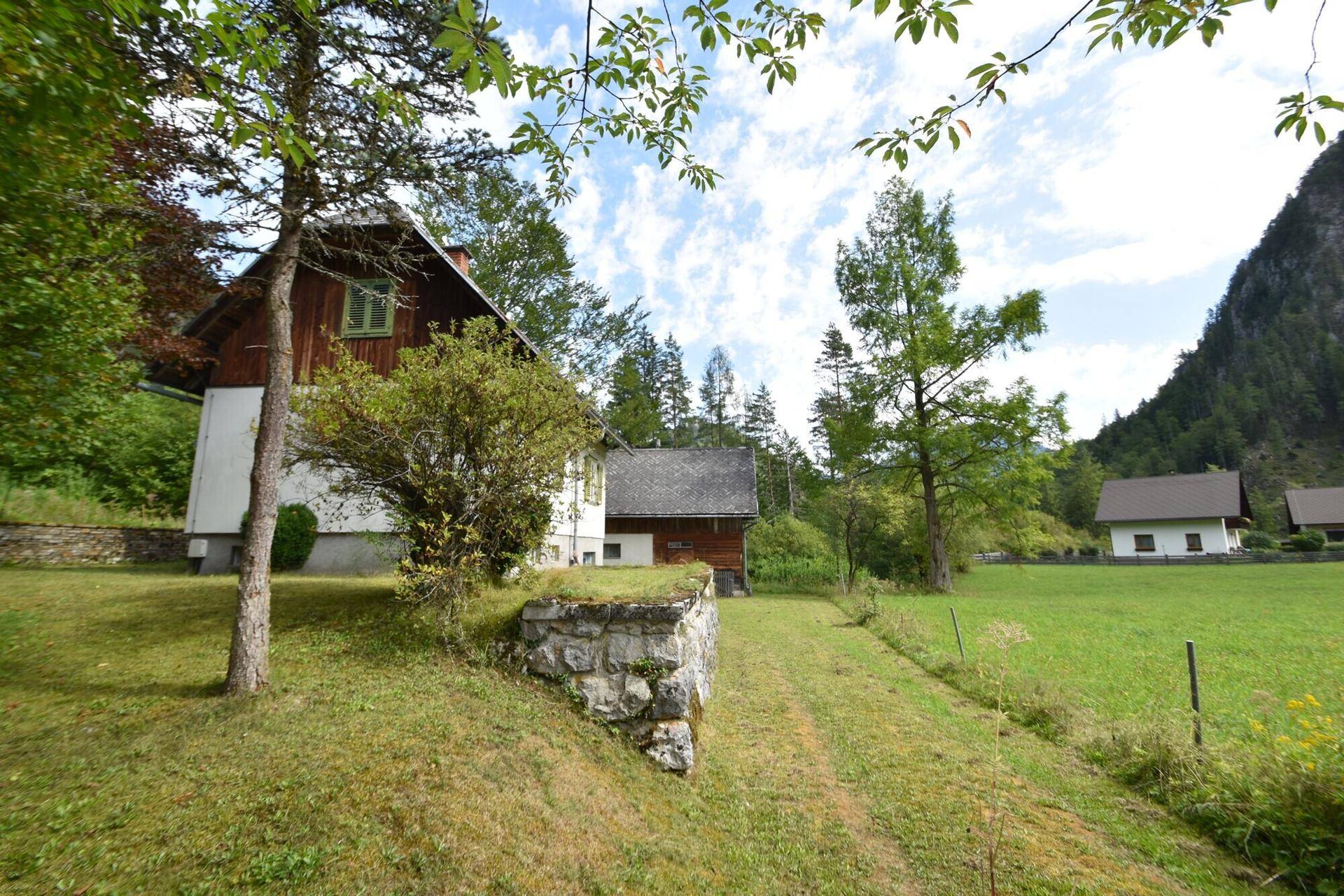 Charmantes Haus mit Steinfundament und grünen Fensterläden, eingebettet in eine natürliche Umgebung.