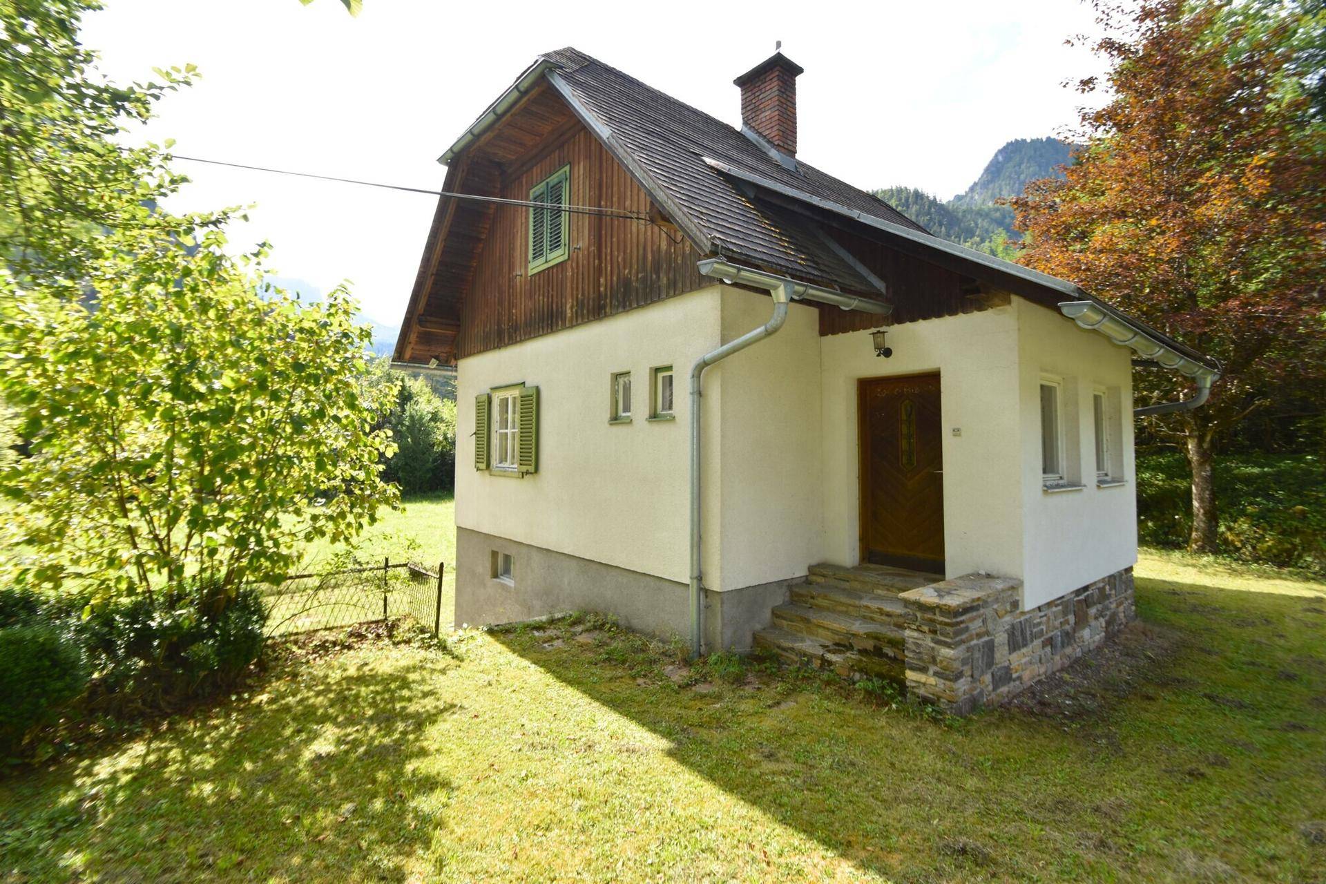 Seitlicher Blick auf ein weißes Haus mit Holzelementen und einem kleinen Eingangsbereich im Grünen.
