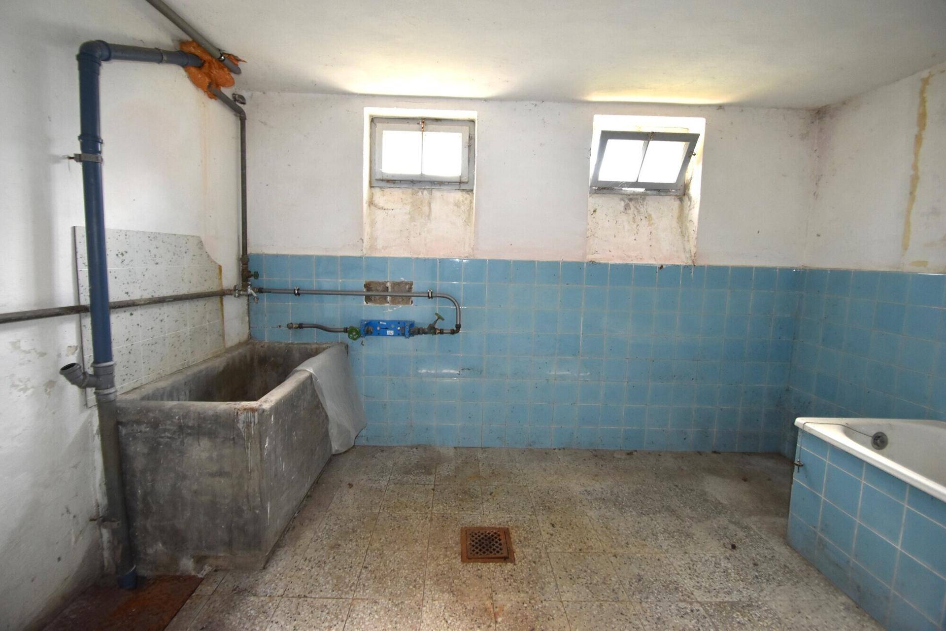 Einfacher Waschraum im Keller mit blauen Fliesen, großem Waschbecken und kleiner Badewanne.
