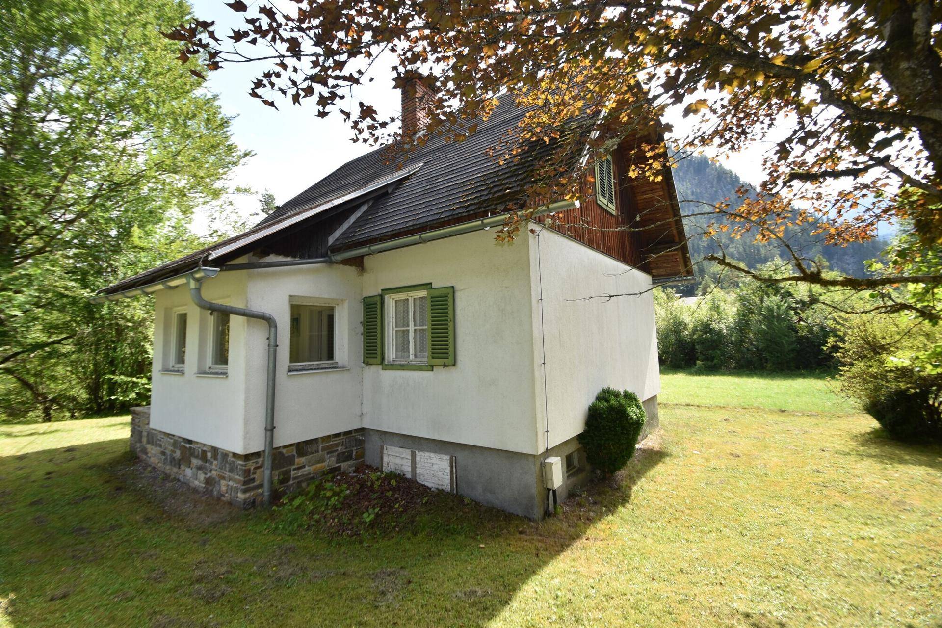 Seitliche Ansicht eines traditionellen Landhauses mit weißer Fassade und grünen Fensterläden.