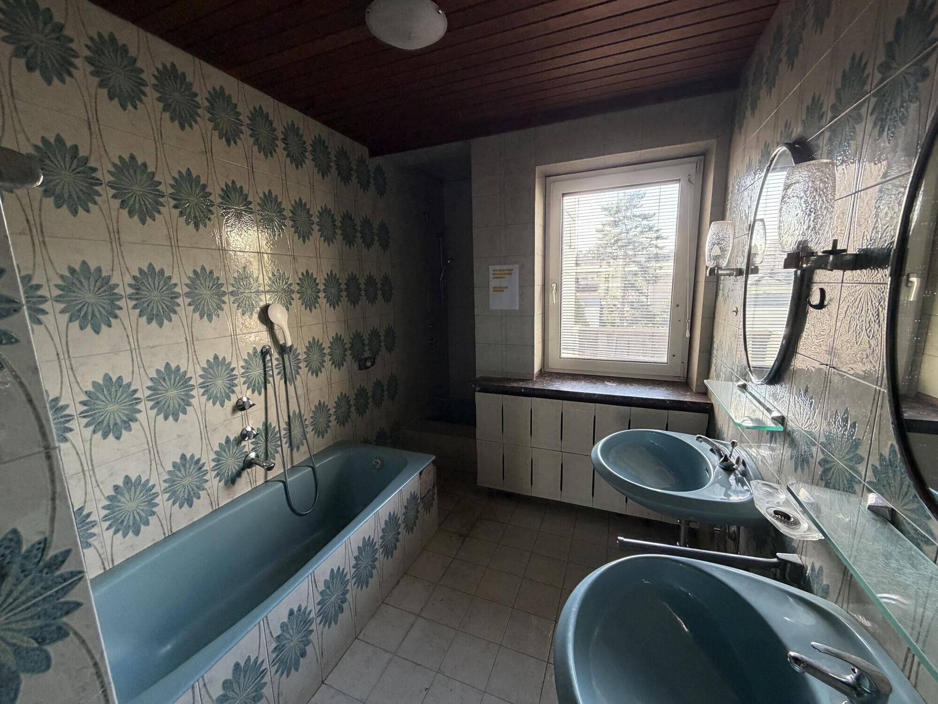 Badezimmer mit blauen Fliesen und zwei Waschbecken, das eine Renovierung benötigt.