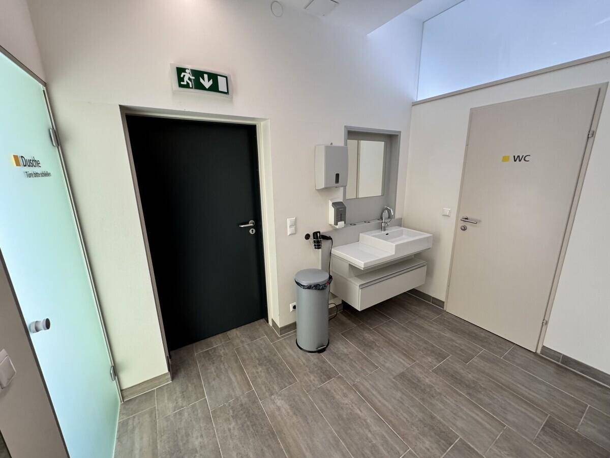 Moderner Umkleidebereich mit Waschbecken, Spiegel und separaten Türen zu Duschen und Toiletten.