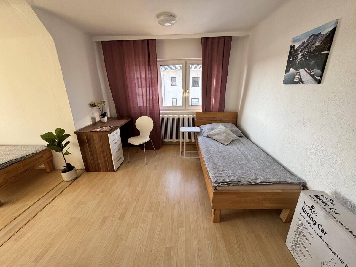 Helles Schlafzimmer mit Einzelbett, Schreibtisch und Parkettboden.