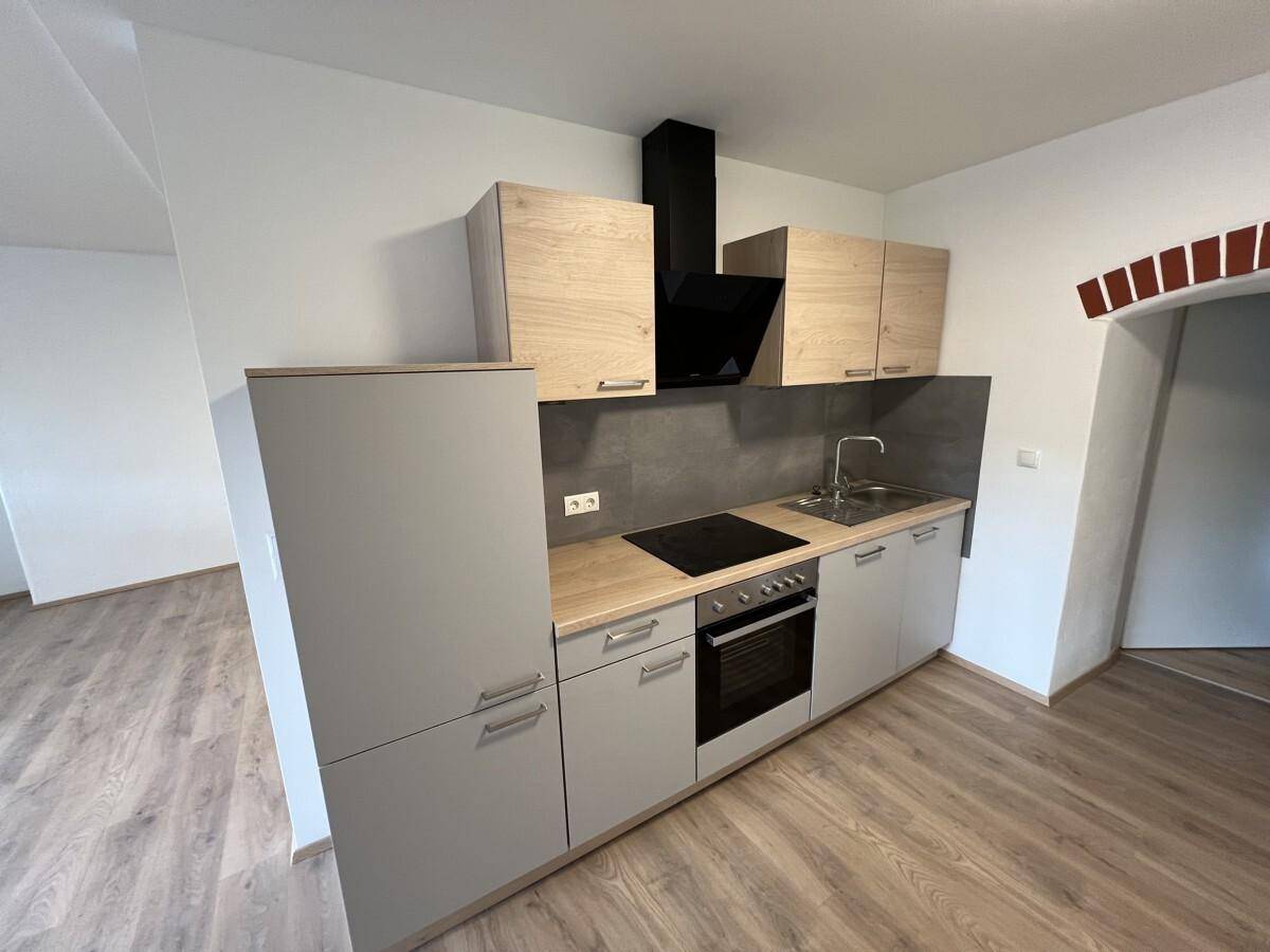Neue Einbauküche mit hellen Holzschränken, grauen Fronten und integrierten Geräten.