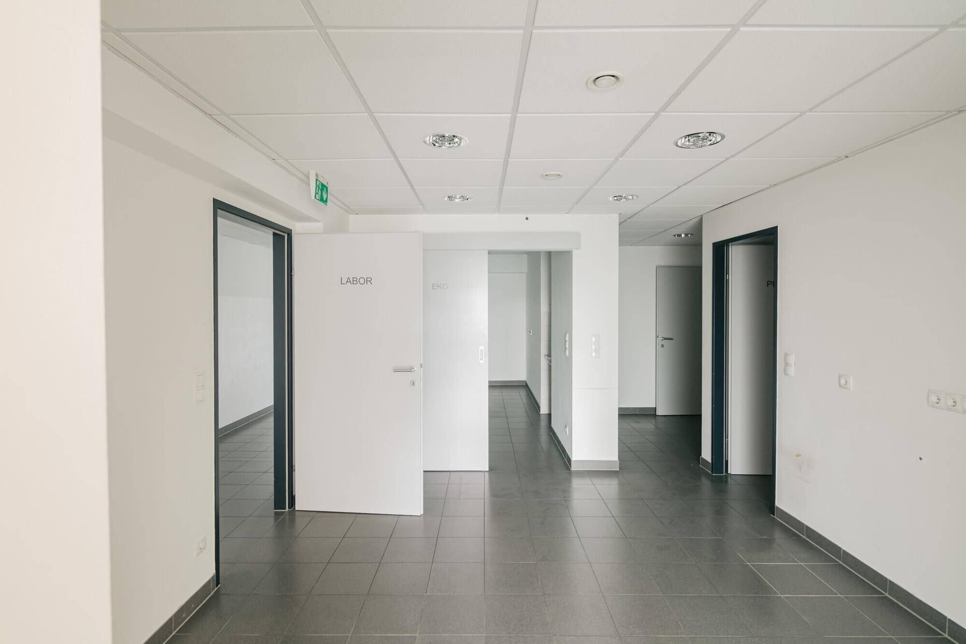 Heller Flur mit mehreren Türen zu verschiedenen Räumen, grauen Fliesen und abgehängter Decke.