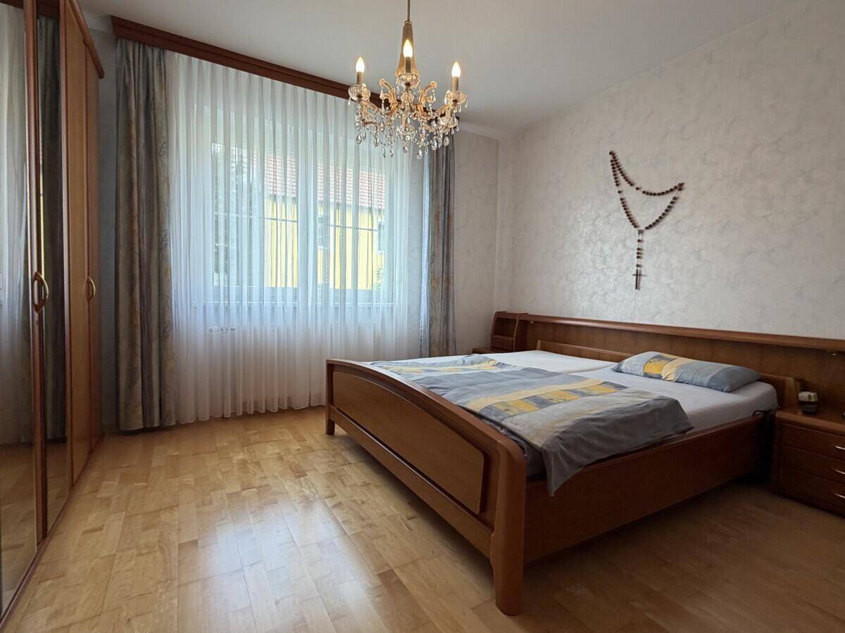 Helles Schlafzimmer mit Holzbett, Parkettboden und großem Fenster mit Vorhängen.