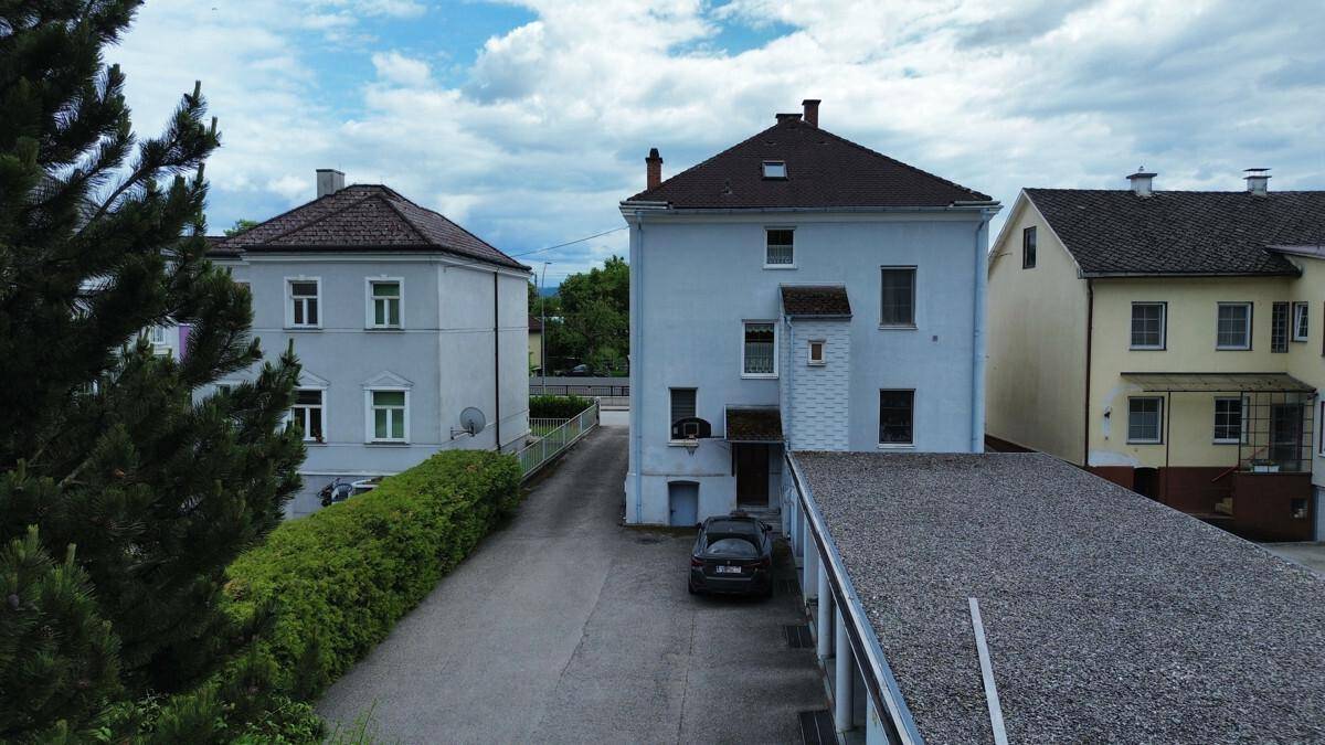 Rückansicht von Wohnhäusern mit einem Carport und grüner Hecke unter bewölktem Himmel.