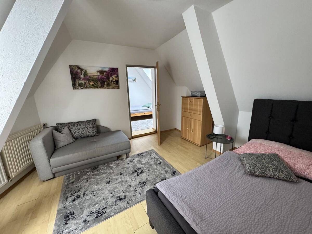 Helles Schlafzimmer im Dachgeschoss mit Bett, Chaiselongue und Holzboden.