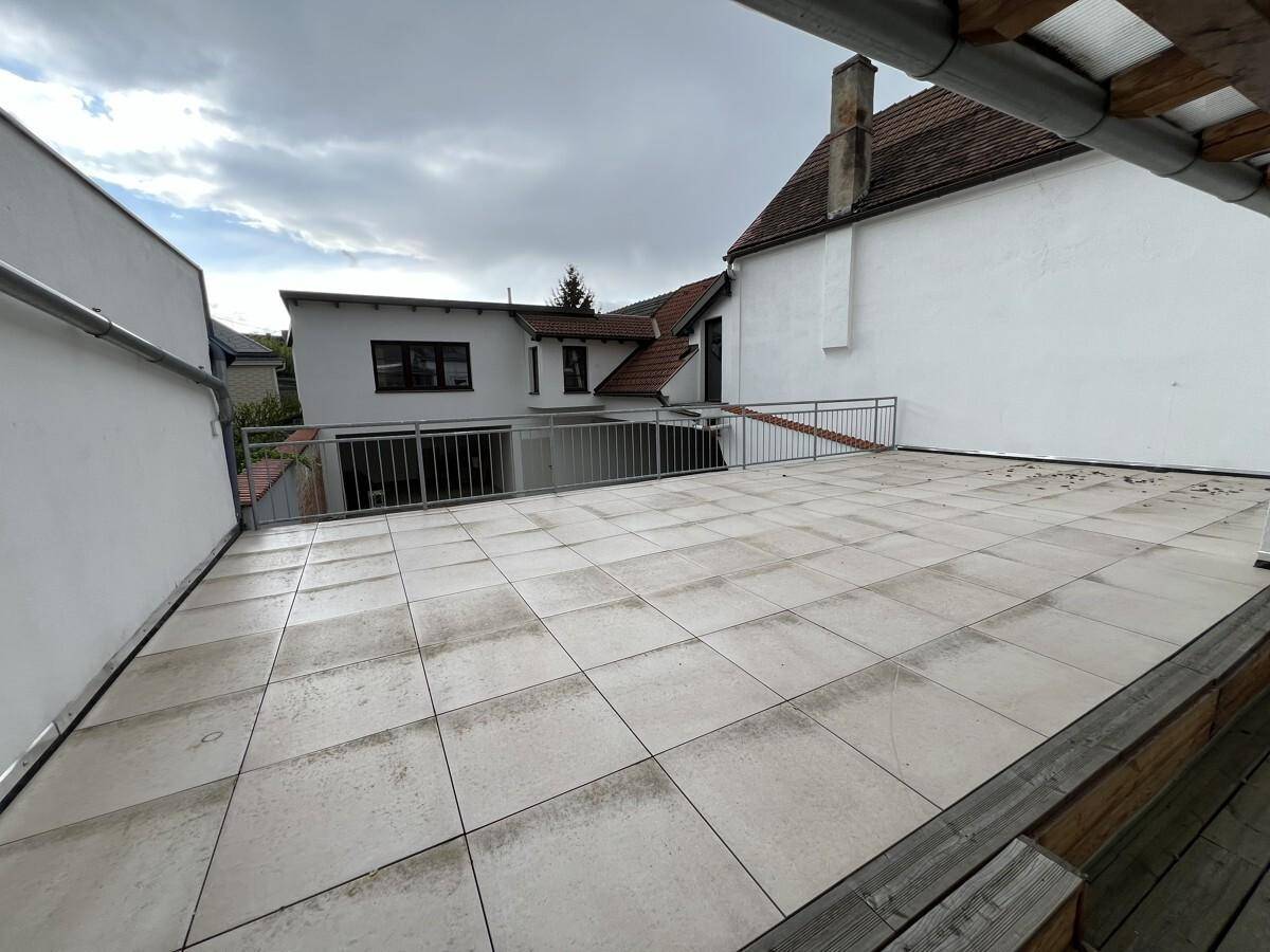 Große geflieste Dachterrasse mit Metallgeländer und Blick auf umliegende Gebäude.