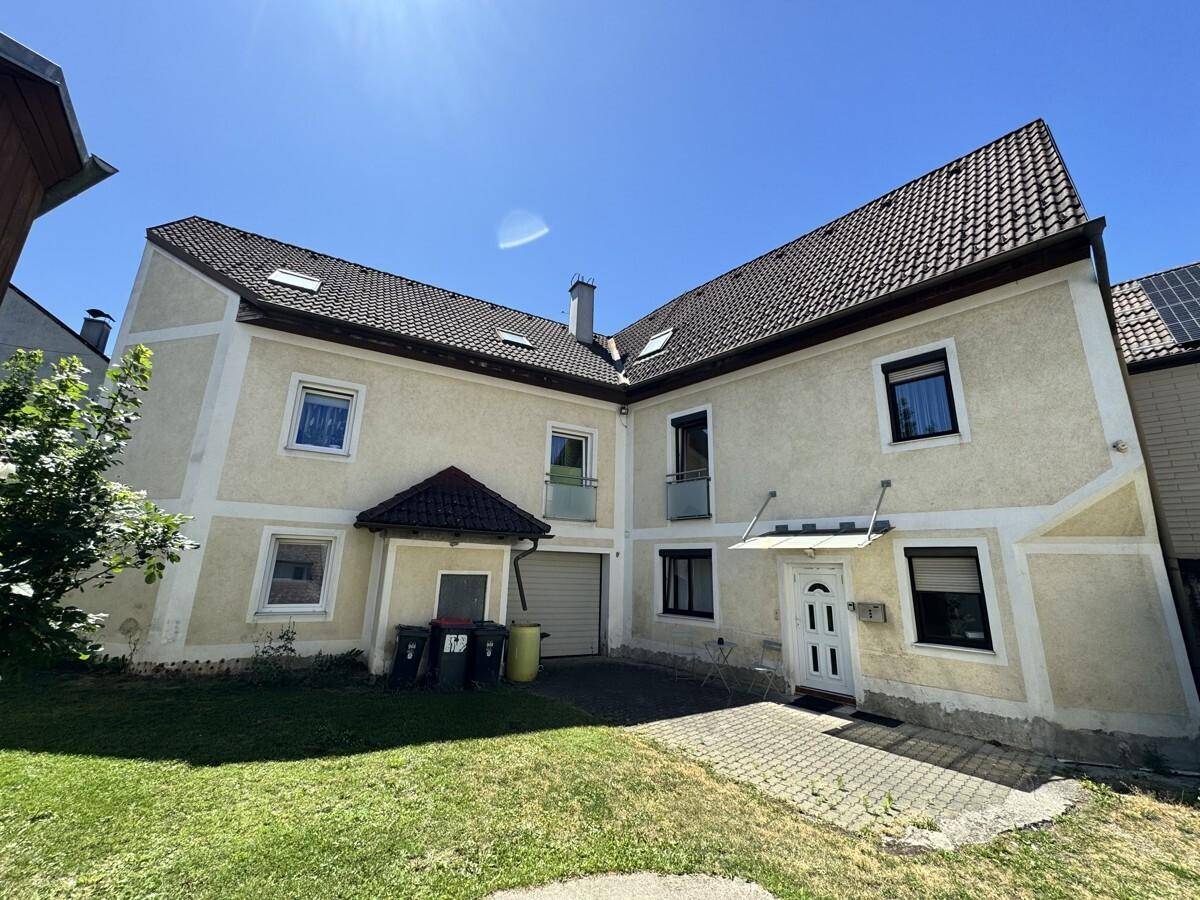 Ansicht des Wohnhauses von außen mit gepflastertem Eingangsbereich und Rasenfläche.