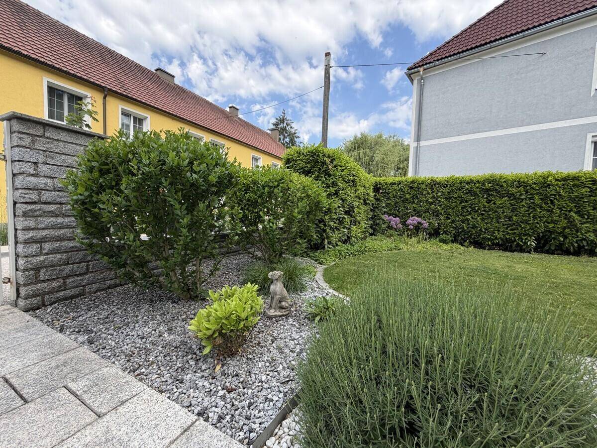 Dekorativer Gartenbereich mit Zierkies, Sträuchern und einer kleinen Gartenfigur.