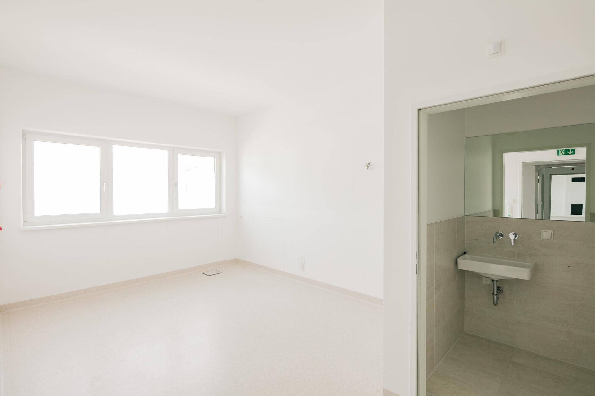 Heller Raum mit Vinylboden und Fenster, daneben ein kleiner Waschbereich mit Waschbecken für den Komfort.