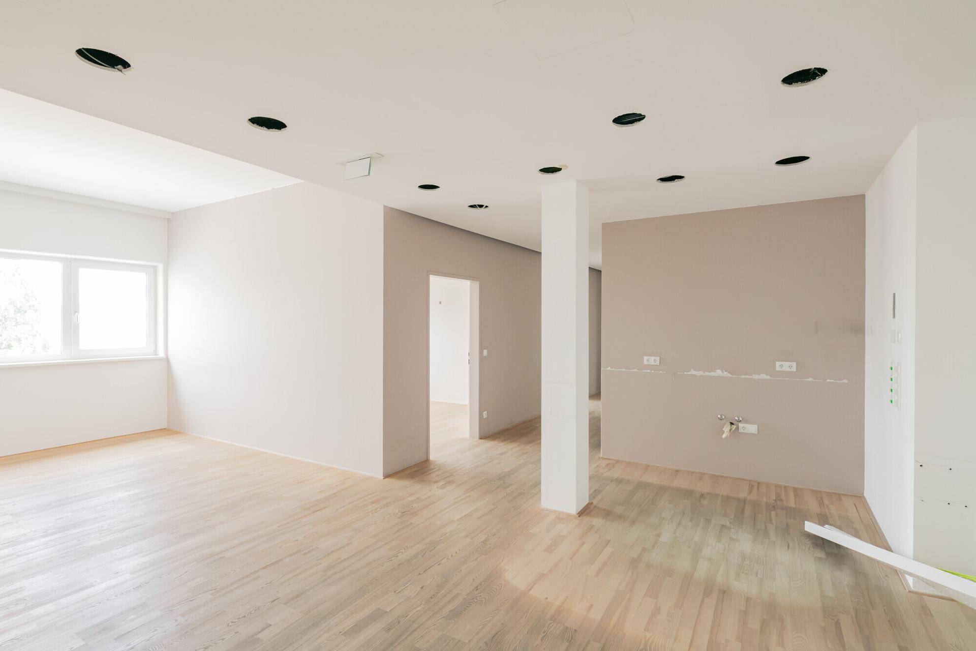 Heller, leerer Raum mit Holzfußboden, Einbaustrahlern und einem Fenster, bereit für die individuelle Einrichtung.