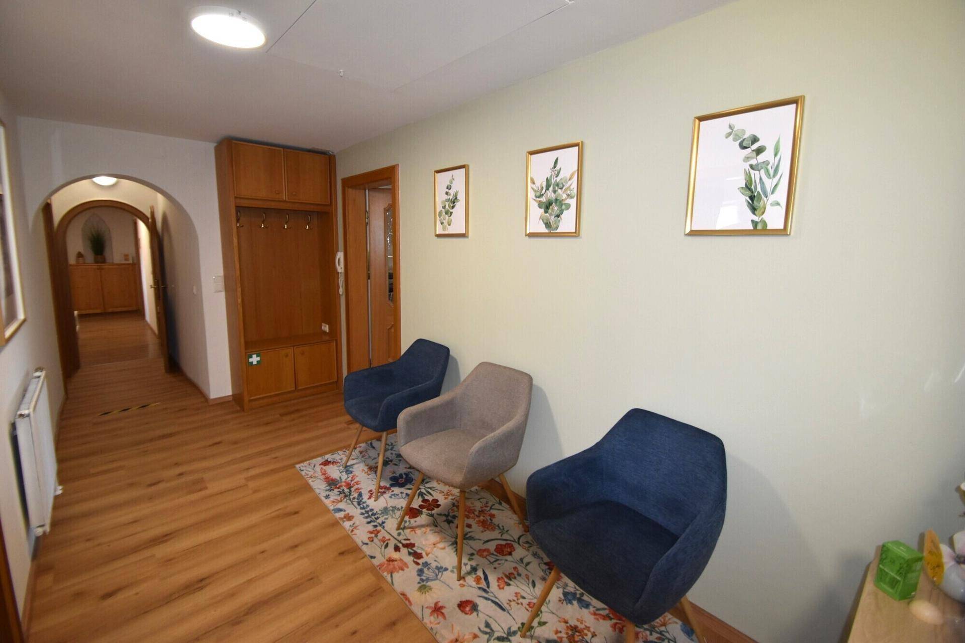 Freundlicher Flur mit Garderobe, Sitzgelegenheiten und Bildern an der hellgrünen Wand.