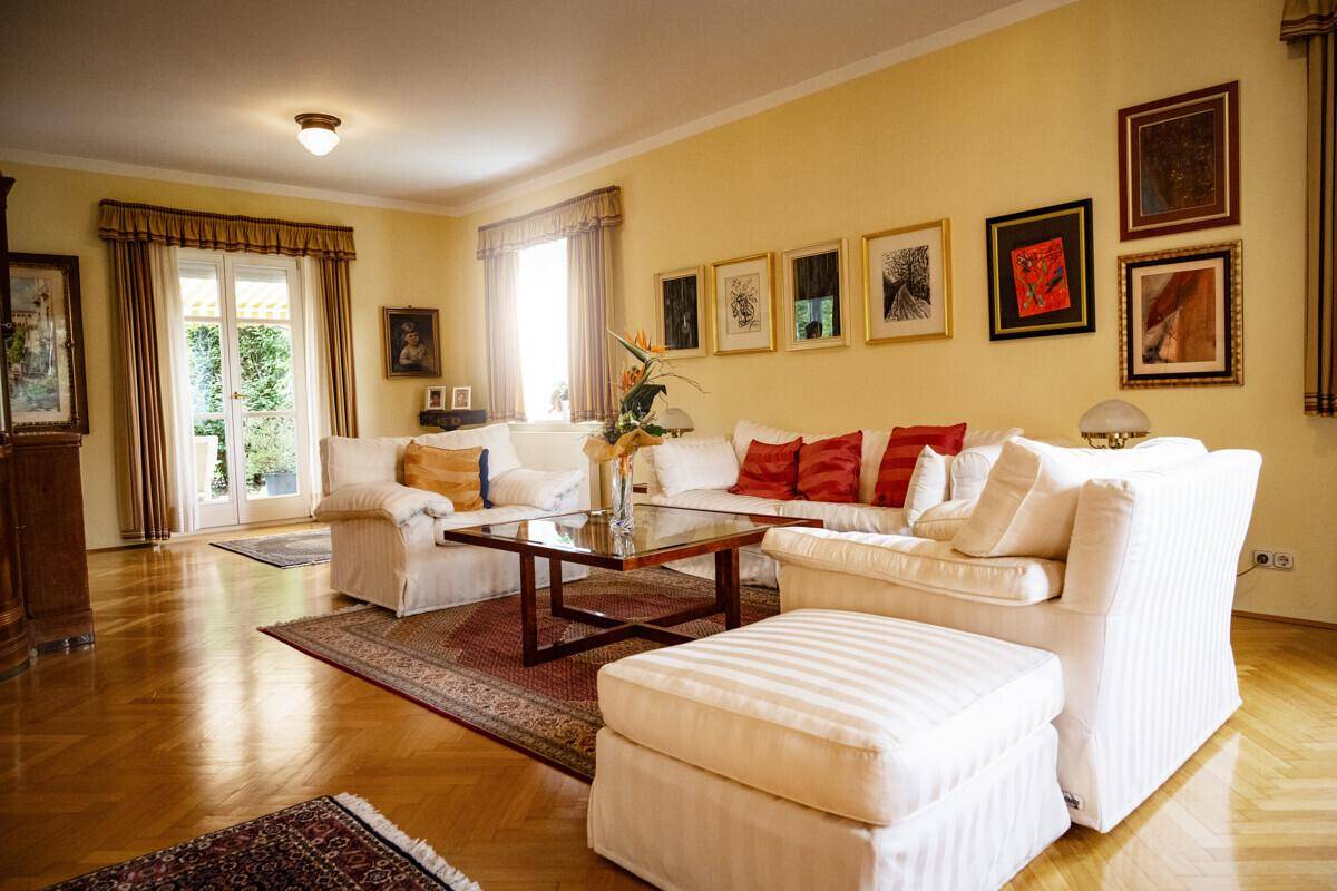 Geräumiges Wohnzimmer mit Parkettboden, eleganten Möbeln und vielen Bildern an der Wand.