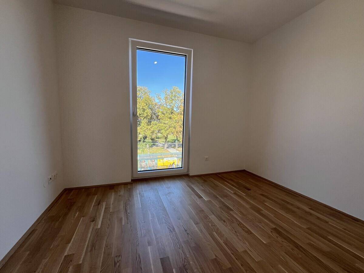 Ruhiges Zimmer mit Parkettboden und großem Fenster, das viel Tageslicht hereinlässt.