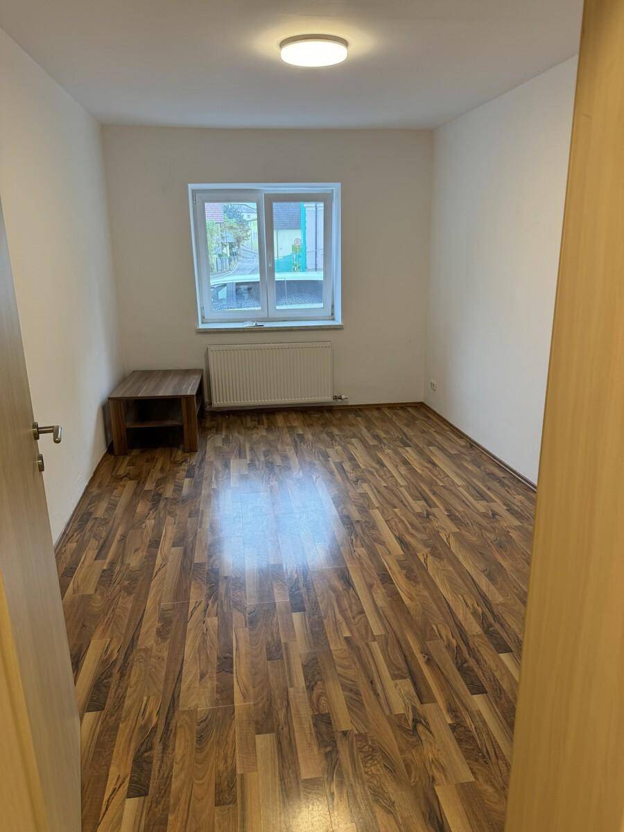 Helles Zimmer mit Laminatboden und einem Fenster, das viel Tageslicht hereinlässt.
