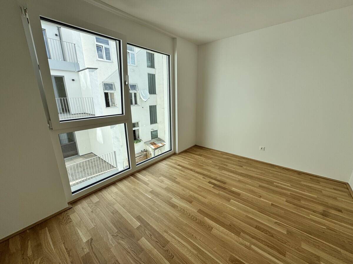 Helles Schlafzimmer mit Eichenparkettboden und großem Fenster mit Blick auf den Innenhof.