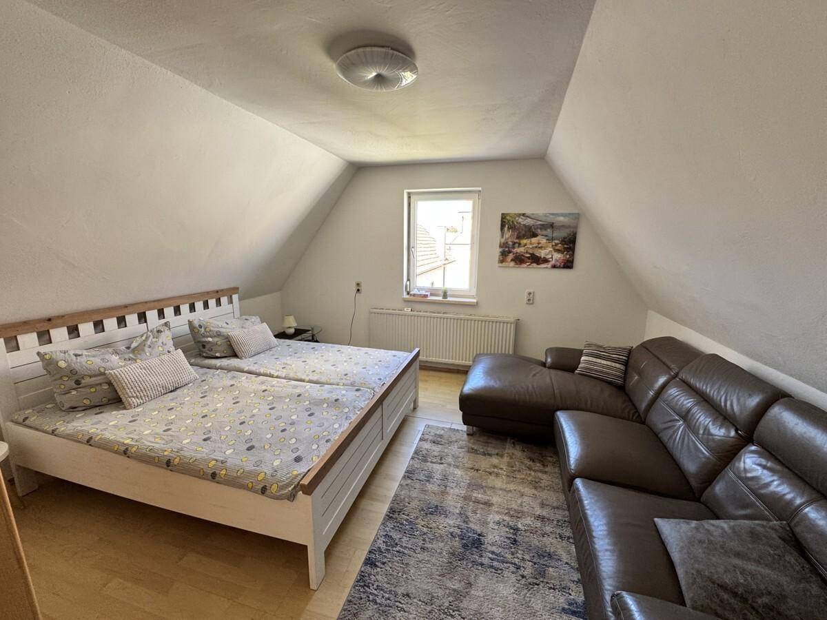 Dachgeschoss-Schlafzimmer mit Doppelbett, Sofa und schrägen Wänden für gemütliches Wohnen.