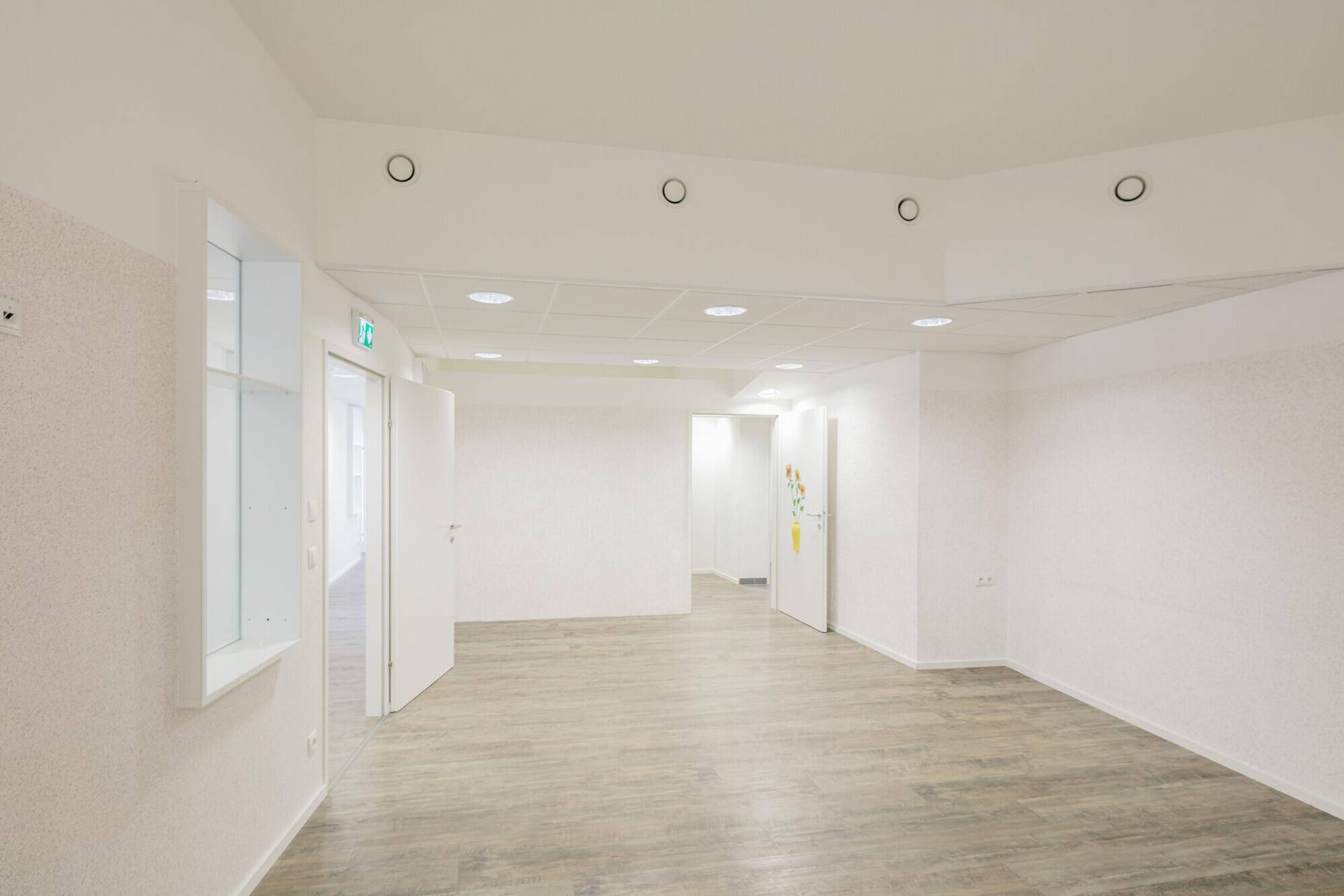 Großer, heller Büroraum mit Holzoptik-Boden und weißen Wänden, ideal für flexible Nutzung.