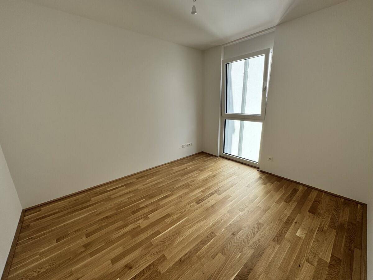 Helles Schlafzimmer mit Eichenparkettboden und hohem Fenster, das viel Tageslicht hereinlässt.