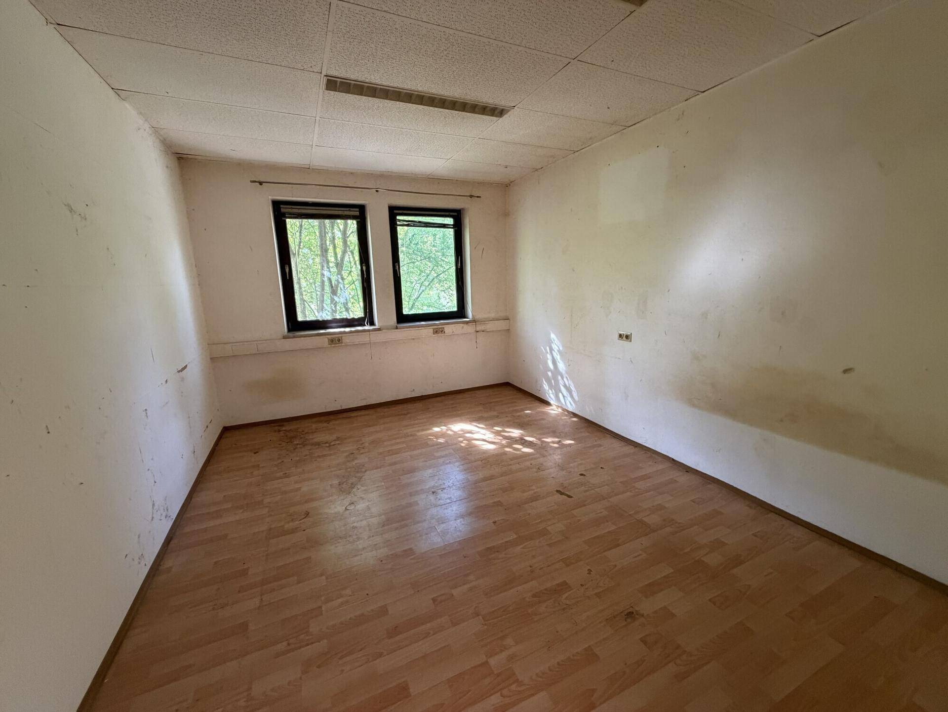 Kleiner Raum mit Laminatboden und zwei Fenstern, die einen Blick ins Grüne bieten.
