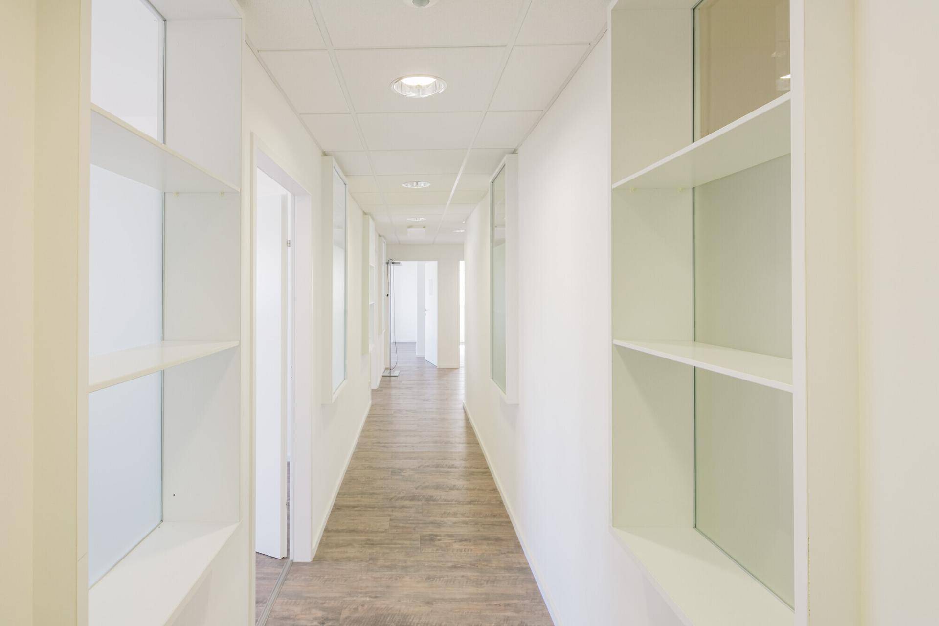 Langer, heller Flur mit Holzoptik-Boden und Einbauregalen, der zu verschiedenen Büroeinheiten führt.
