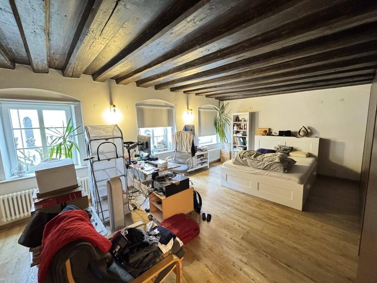 Helles Schlafzimmer mit Holzbalkendecke, Holzboden und zwei Fenstern.