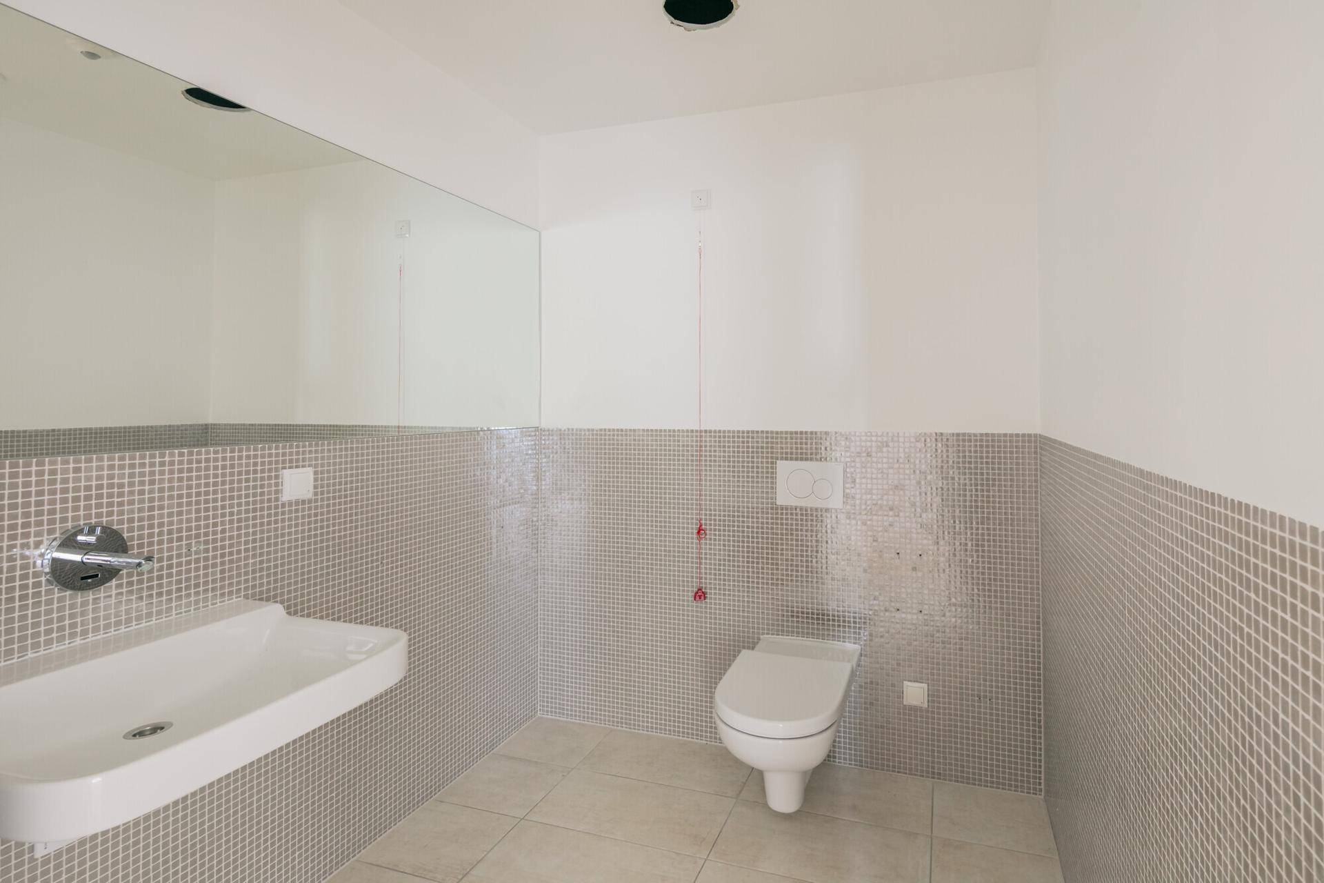 Modernes WC mit wandhängender Toilette, Waschbecken und grauen Mosaikfliesen an den Wänden.
