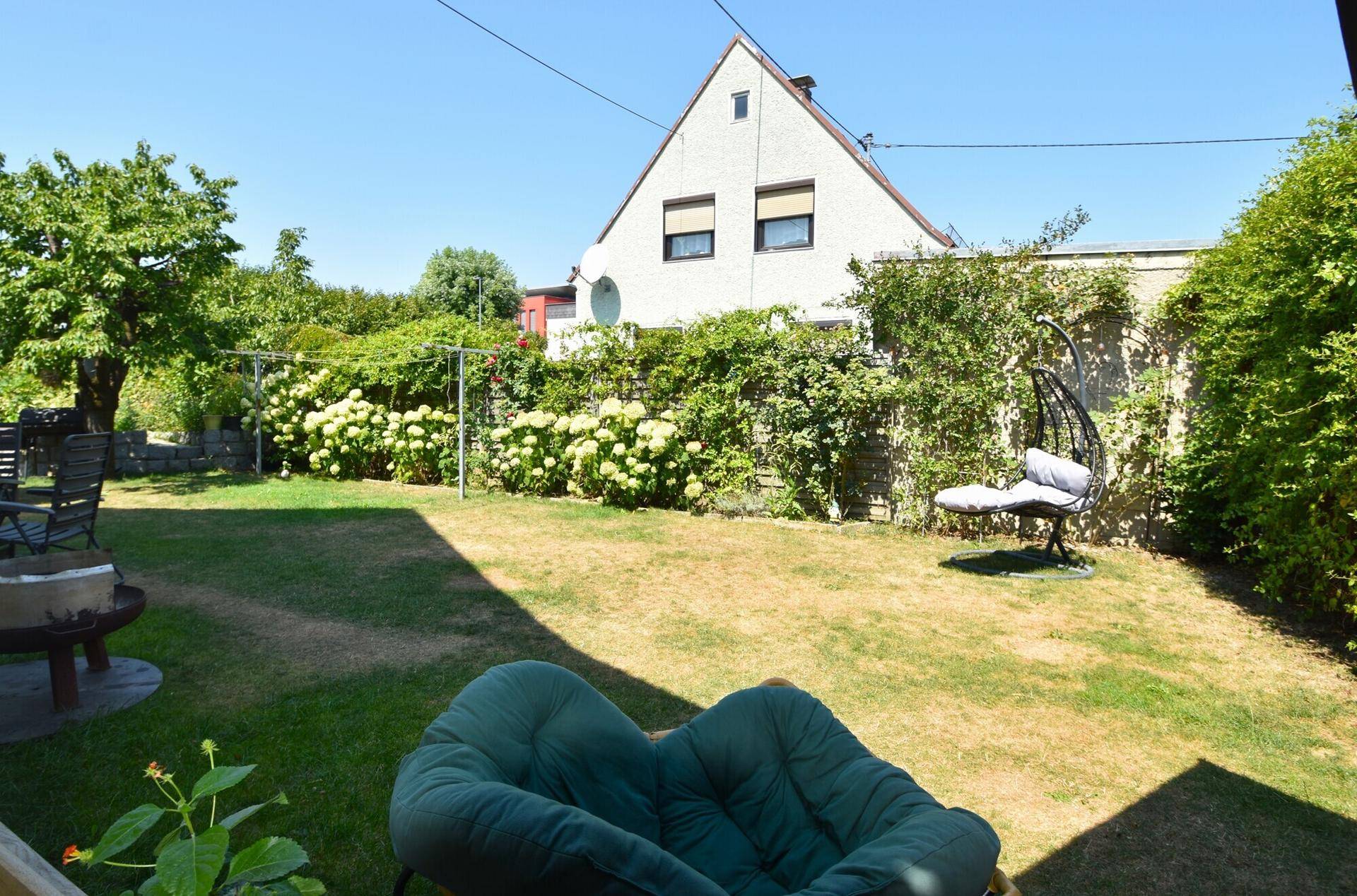Großer Garten mit Rasenfläche, Blumen und Sitzgelegenheiten im Freien.