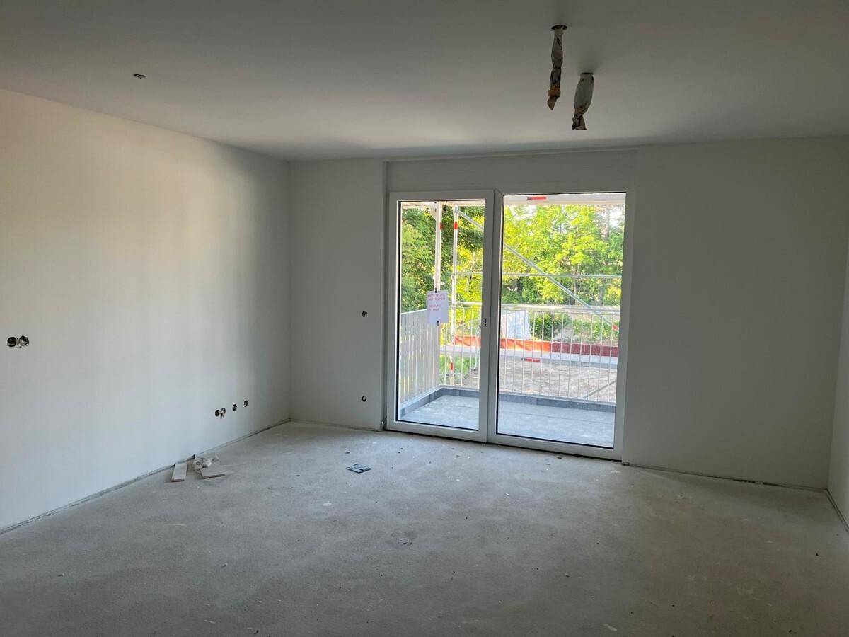 Heller, unmöblierter Raum mit Zugang zu einem Balkon oder einer Terrasse, bereit für den Innenausbau.