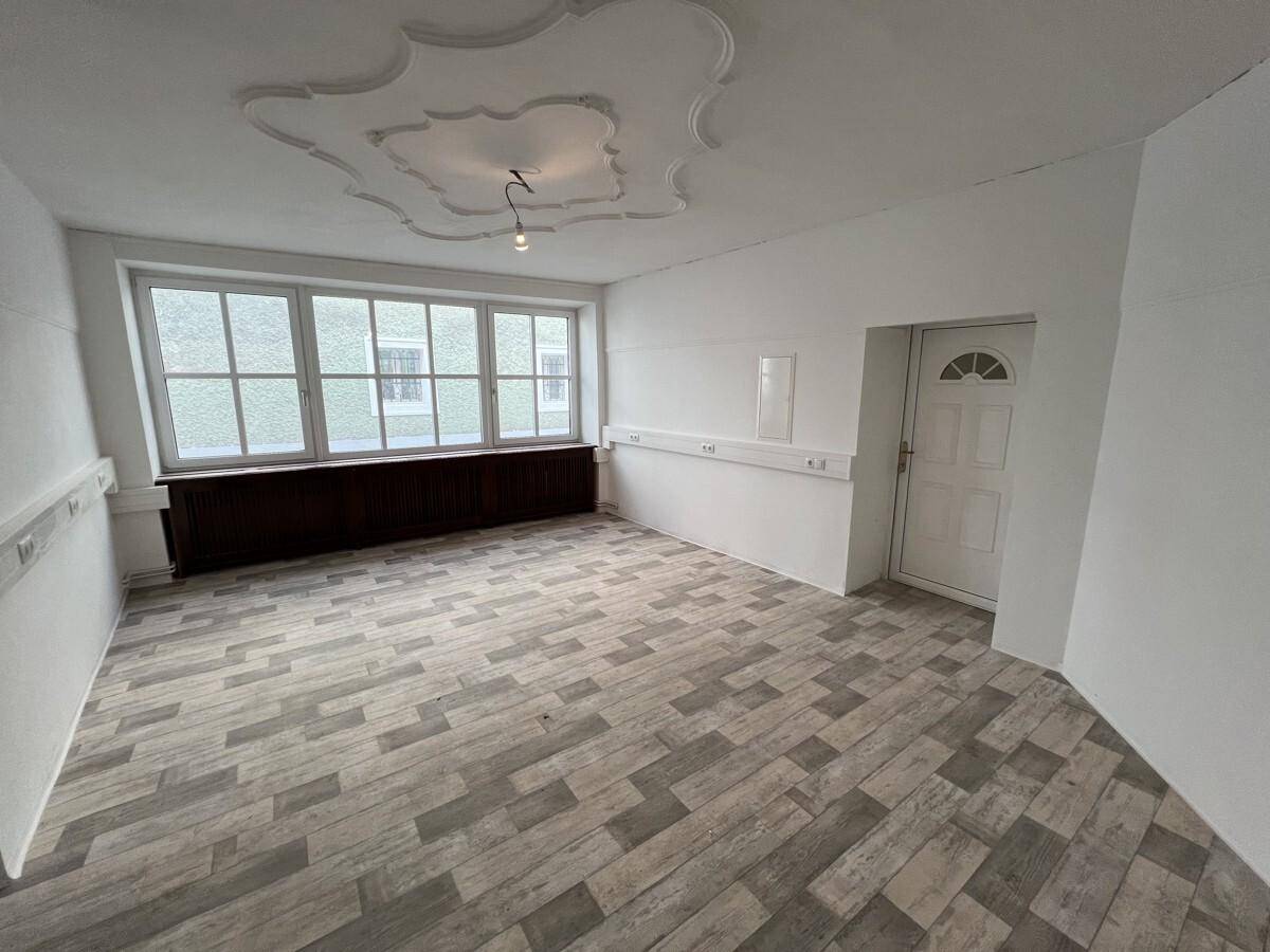 Geräumiger Raum mit Laminatboden, großen Fenstern und dekorativer Stuckdecke.