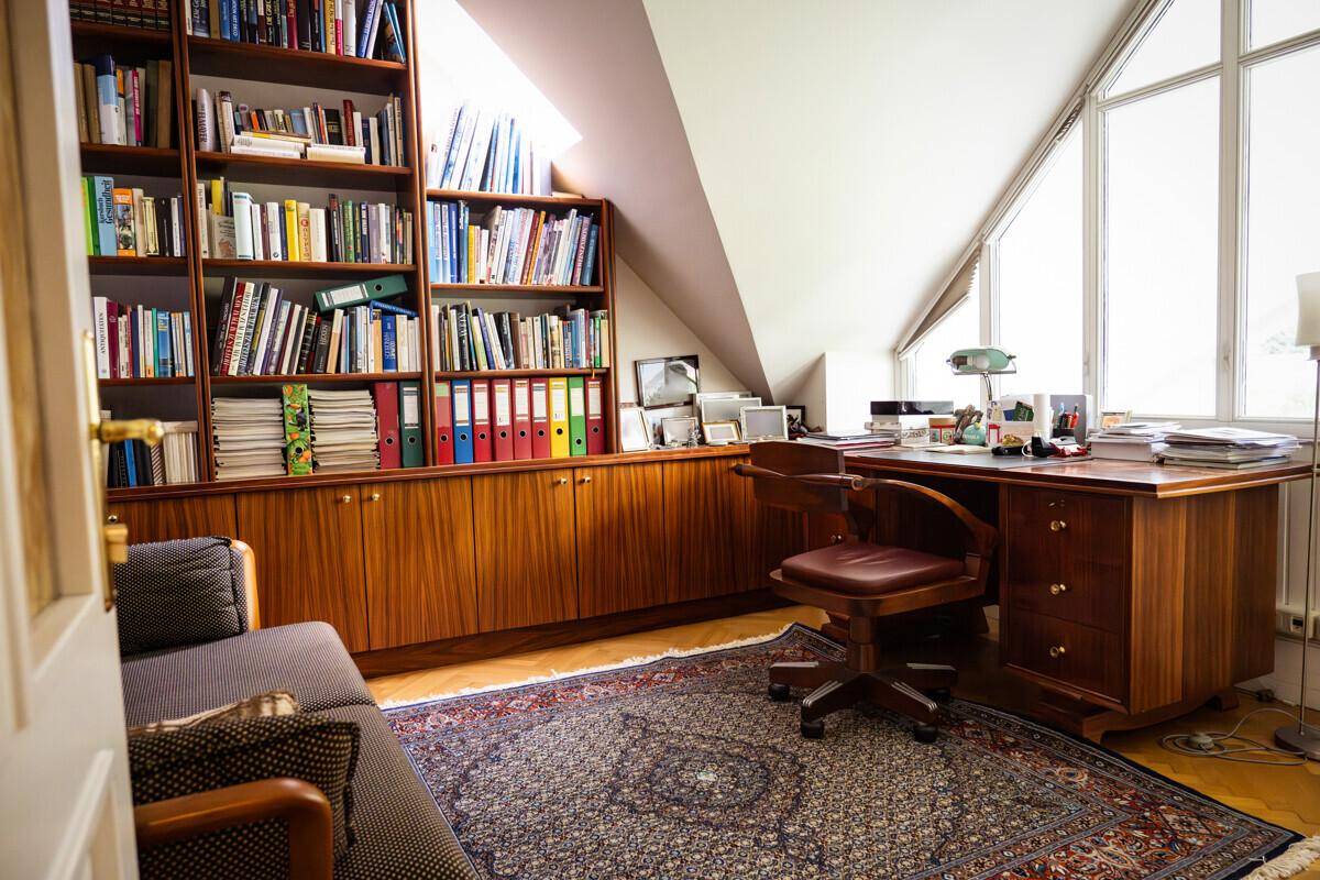 Geräumiges Büro mit großem Schreibtisch, Bücherregalen und viel Tageslicht durch große Fenster.